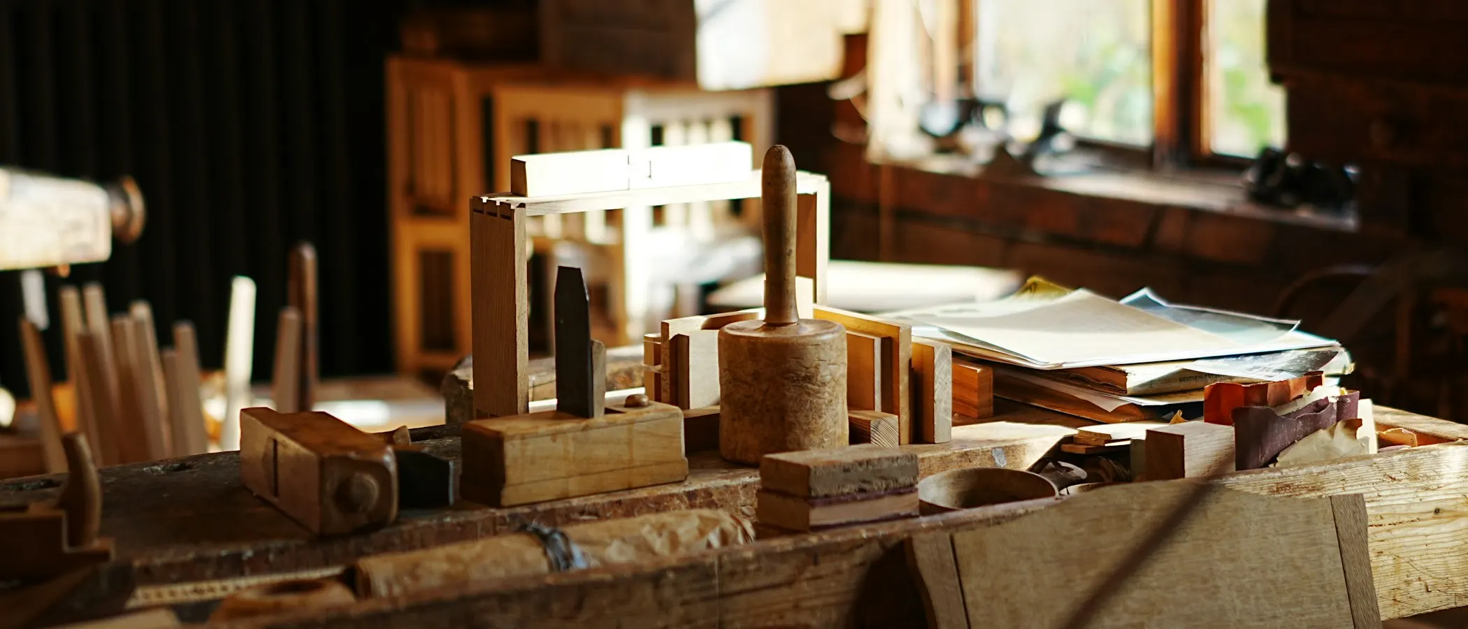 Hobel, Holzklüpfel und Werkstücke auf einer Hobelbank in einer Schreinerwerkstatt im warmen Fensterlicht.